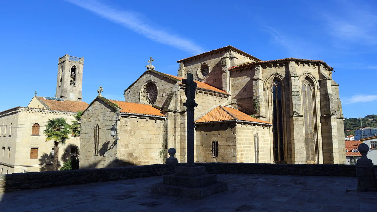 La iglesia gótica de San Francisco de Betanzos vista desde la calle, con el campanario a un lado y los tejados del pueblo detrás.