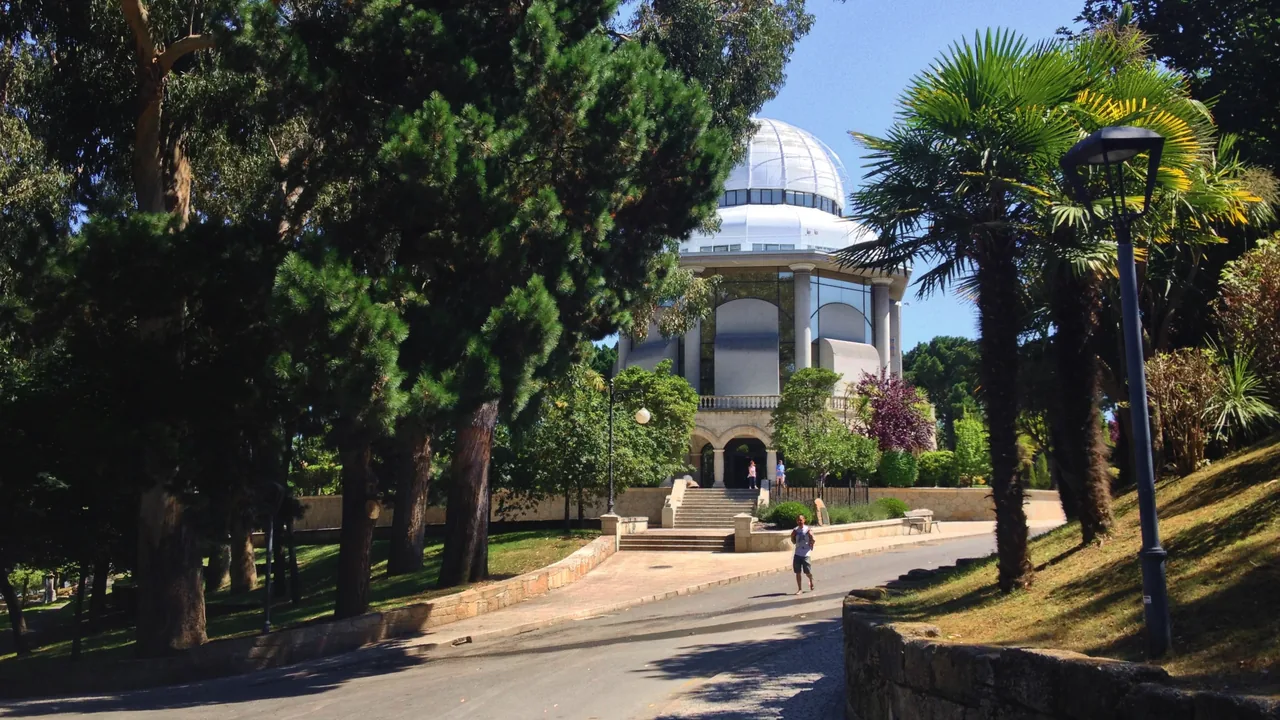 La Casa de las Ciencias entre los árboles del parque de Santa Margarita, con su galería de arcos en la planta baja y la cúpula del planetario arriba.