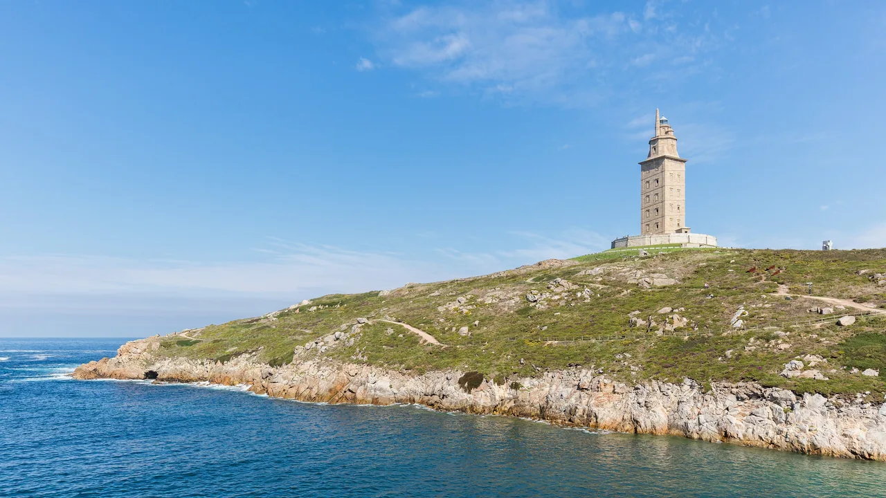 La Torre de Hércules en lo alto del promontorio verde, con el acantilado y el Atlántico batiendo abajo.