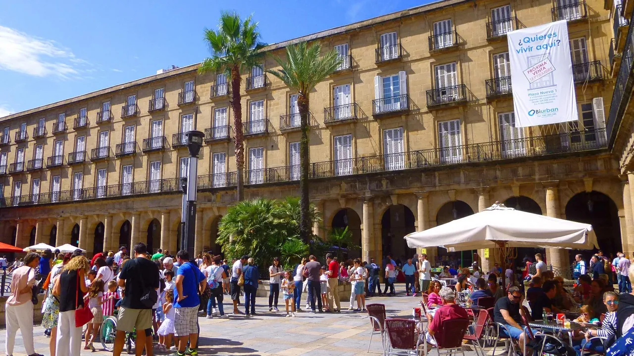 Los soportales de la Plaza Nueva de Bilbao con las terrazas ocupadas y gente cruzando la plaza.