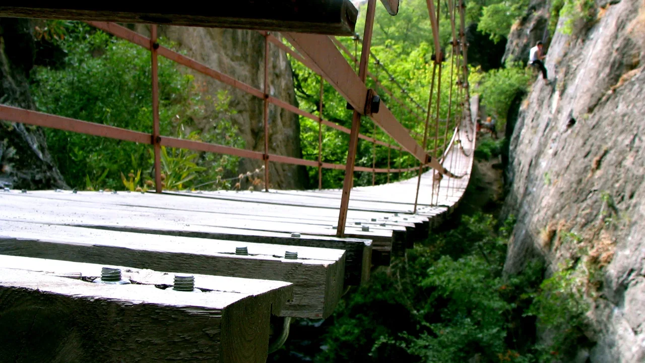El puente colgante de tablas de Los Cahorros visto desde el estribo, con los cables tensados y la pared de caliza del desfiladero al lado.