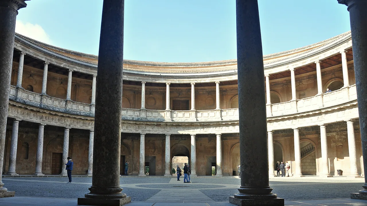 El patio circular del Palacio de Carlos V visto entre dos columnas, con sus dos pisos de arcos y unas pocas personas cruzándolo.
