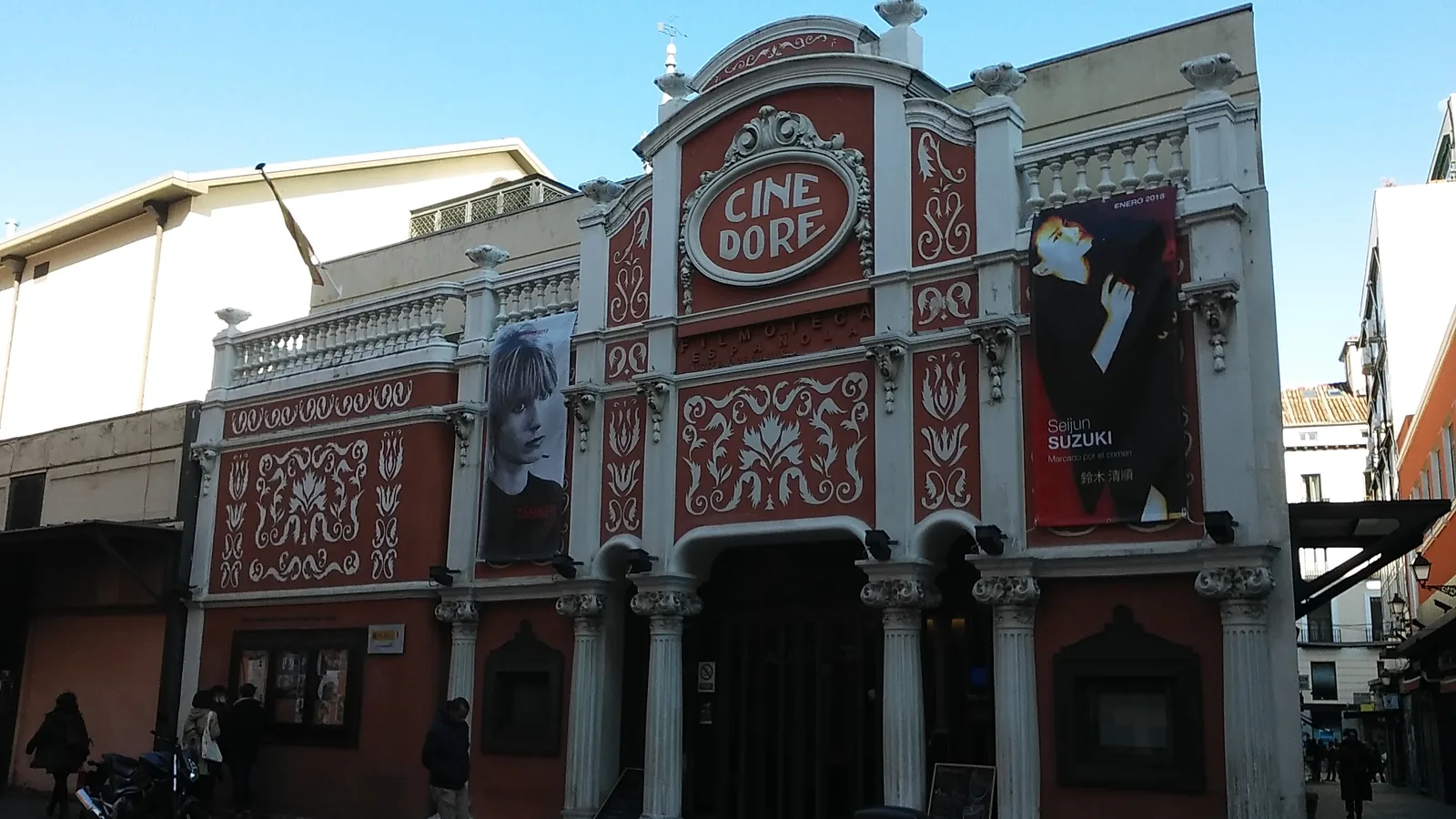 Fachada modernista roja y blanca del Cine Doré en Madrid, con el letrero de la Filmoteca Española y gente en la entrada.