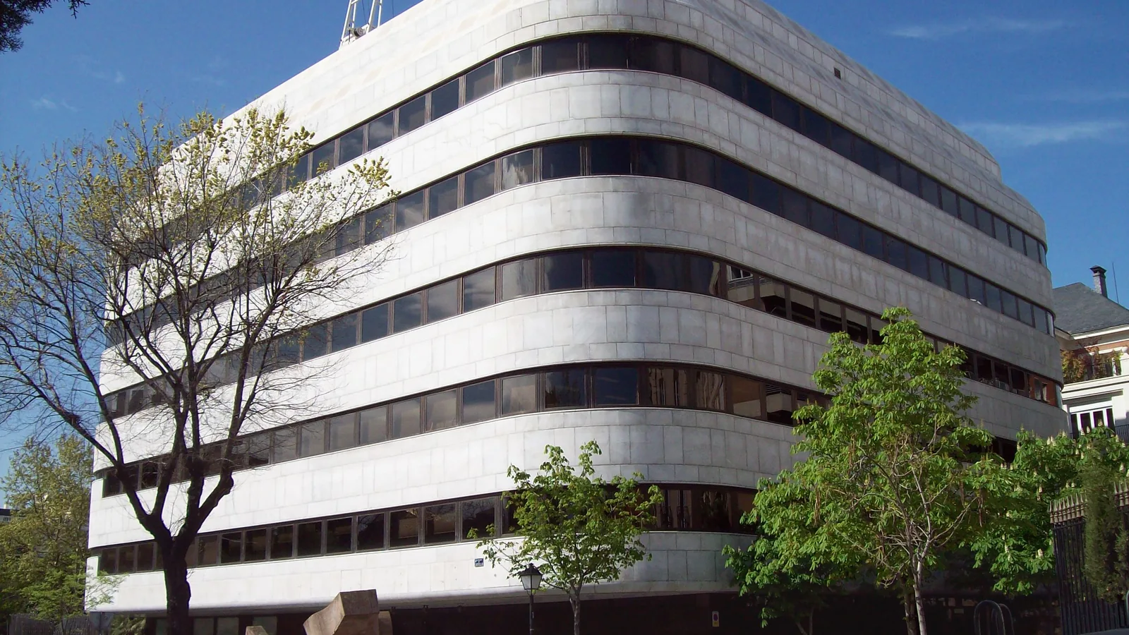 Edificio de mármol blanco de la Fundación Juan March en la calle Castelló de Madrid, entre árboles y cielo despejado.