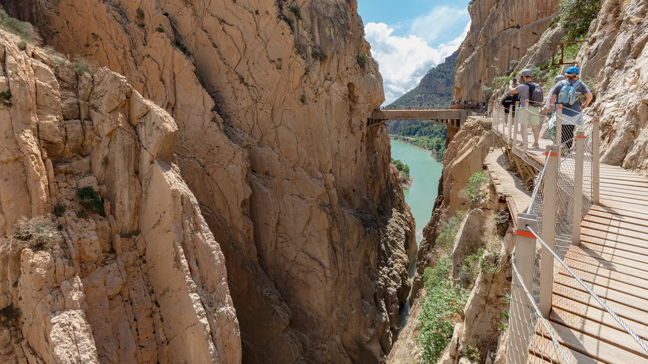 La pasarela de madera del Caminito del Rey pegada a la pared del desfiladero, con excursionistas caminando en fila india sobre el río.