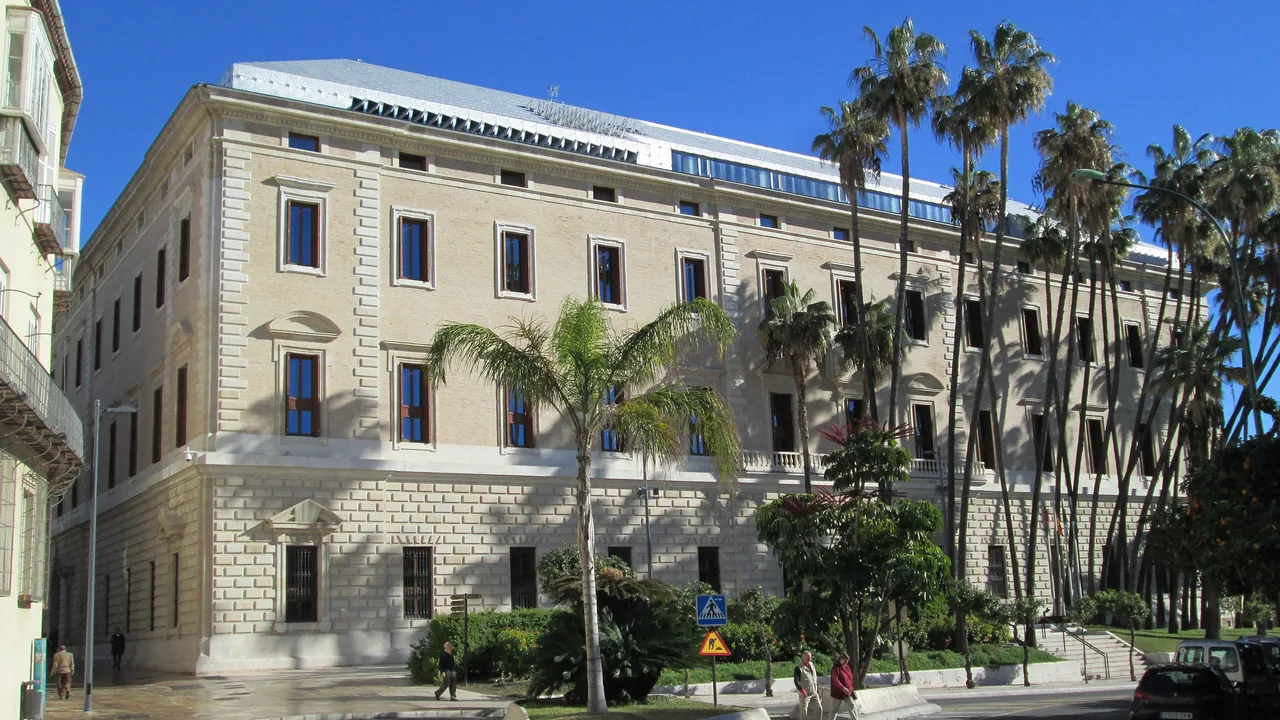 La fachada neoclásica del Palacio de la Aduana, sede del Museo de Málaga, con las palmeras del Parque delante.
