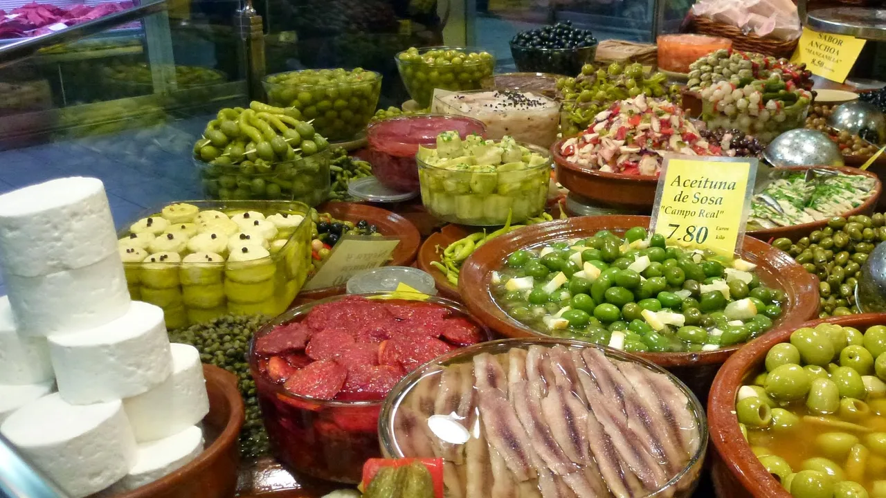 Un puesto del Mercat de l'Olivar con quesos, aceitunas, encurtidos y anchoas servidos en fuentes de barro.