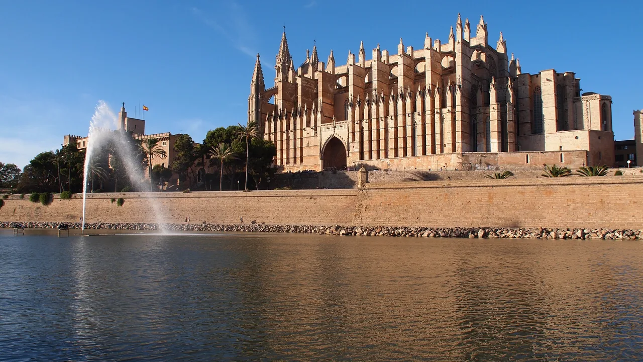 El lago del Parc de la Mar con su surtidor y, tras la muralla, la Seu y el Palau de l'Almudaina en piedra dorada.
