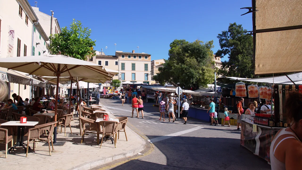 Día de mercado en Sineu: las mesas de un bar a la sombra a un lado de la calle y las paradas del mercado al otro.