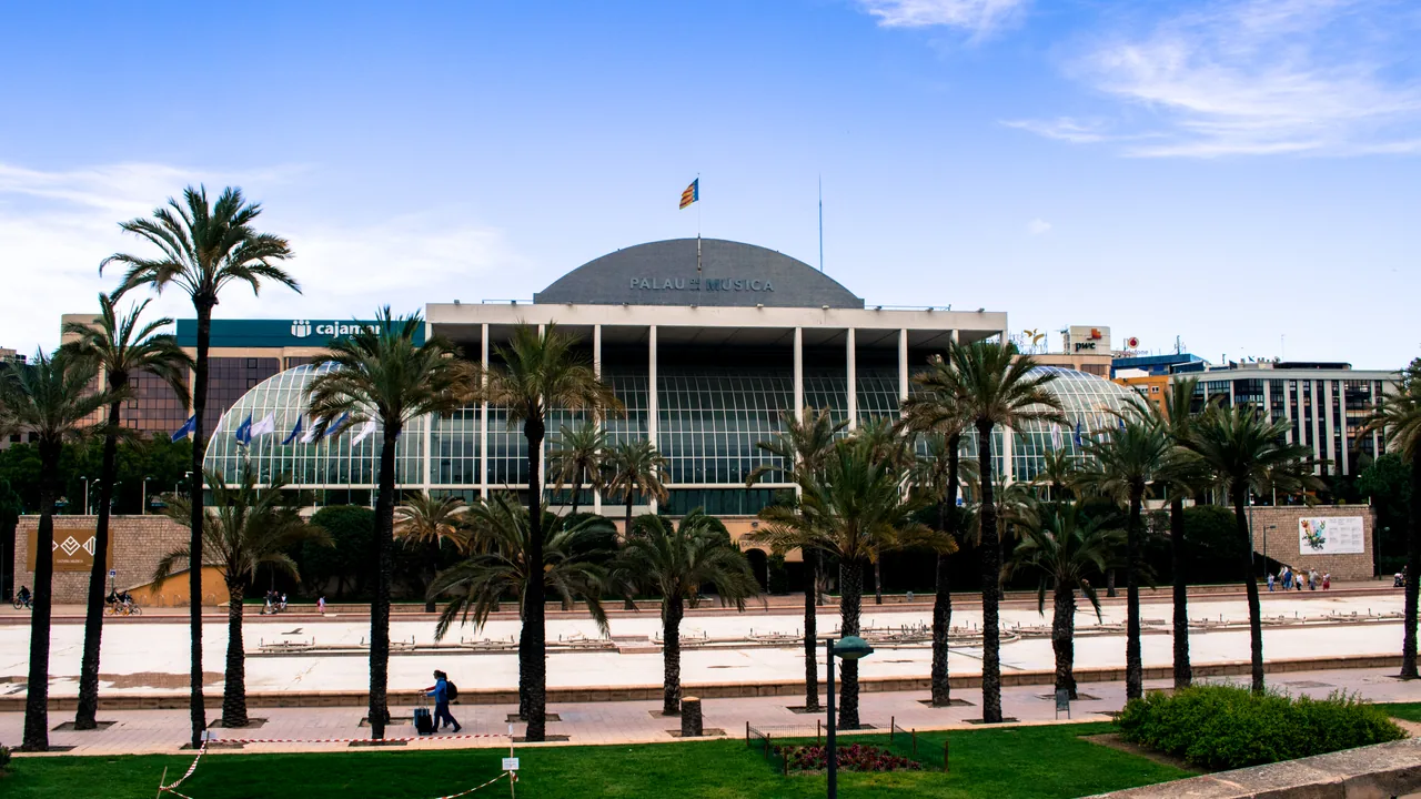 La cúpula acristalada del Palau de la Música de València rodeada de palmeras y jardín.
