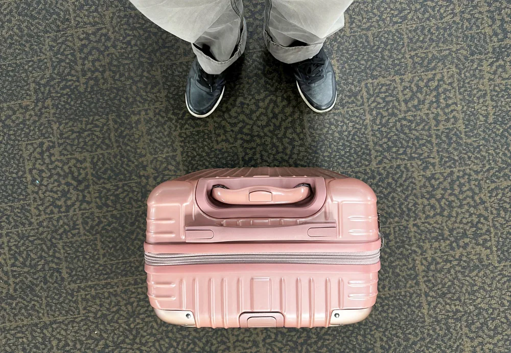 POV de pies y maleta rosa en suelo de aeropuerto — viajar solo sin suplemento individual unente